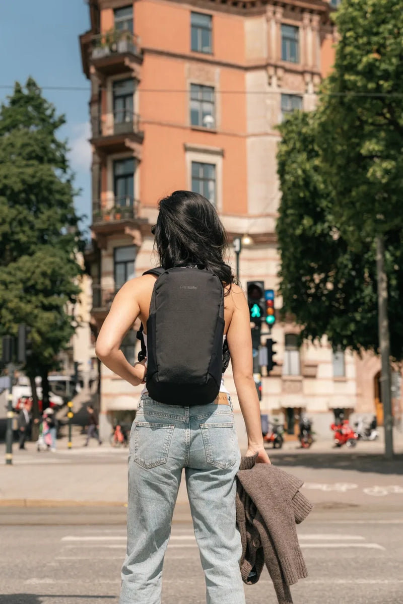Pacsafe V Tech 12L Anti-Theft Backpack in Black, worn on both shoulders by a woman waiting at a city crossing