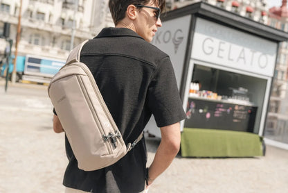 Pacsafe V Tech Anti-Theft 10L Sling Pack in Beige, worn across the back by a man walking past a gelato kiosk