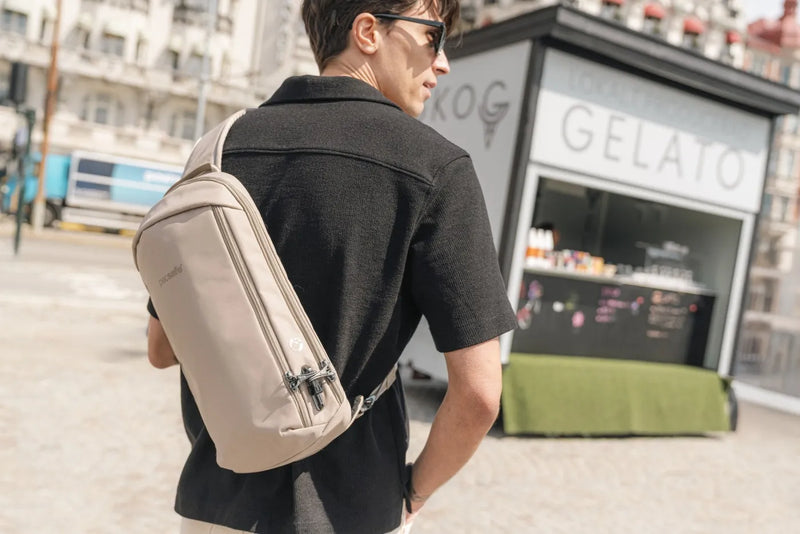 Pacsafe V Tech Anti-Theft 10L Sling Pack in Beige, worn across the back by a man walking past a gelato kiosk