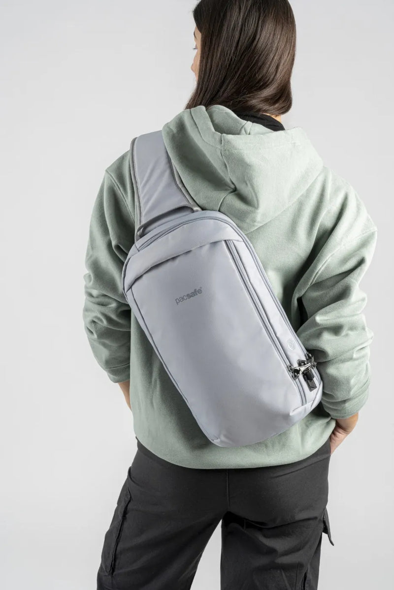 Pacsafe V Tech Anti-Theft 10L Sling Pack in Digital Grey, worn across the back over a green hoodie, seen from behind