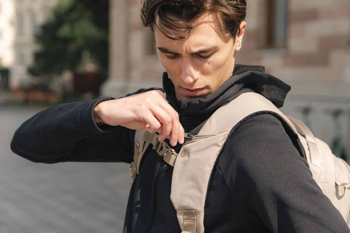 Pacsafe V Tour 26L Anti-Theft 16" Laptop Backpack in Beige, chest strap being clipped shut by a man on a city street