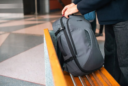 Pacsafe Venturesafe EXP45 Anti-Theft 45L Carry-on Travel Pack in Slate, lifted by its handle from a bench at a station