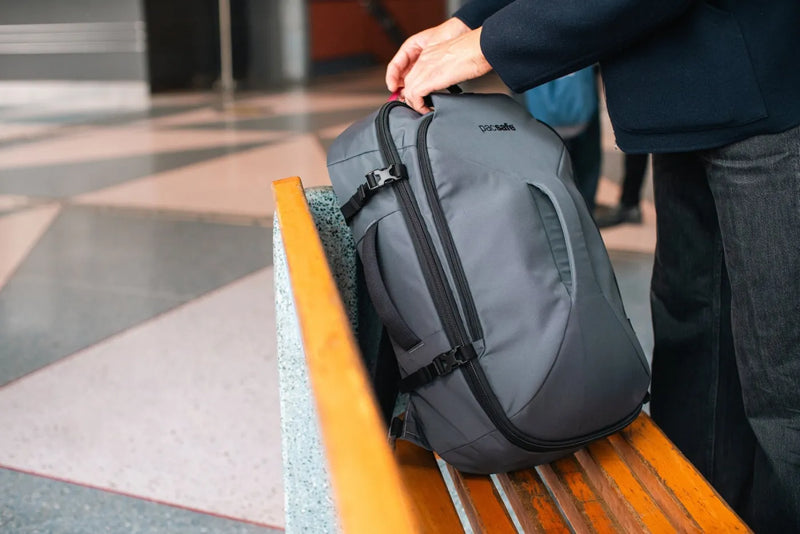 Pacsafe Venturesafe EXP45 Anti-Theft 45L Carry-on Travel Pack in Slate, lifted by its handle from a bench at a station