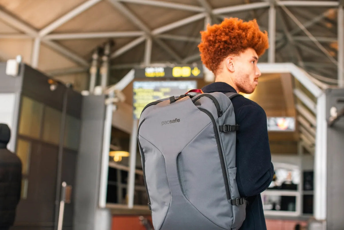 Pacsafe Venturesafe EXP45 Anti-Theft 45L Carry-on Travel Pack in Slate, worn on both shoulders by a man in a station departure hall
