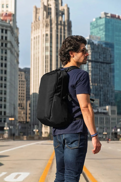 Pacsafe Vibe 25 - Anti-Theft 25L Laptop Daypack in Jet Black, worn on both shoulders by a man walking a downtown street