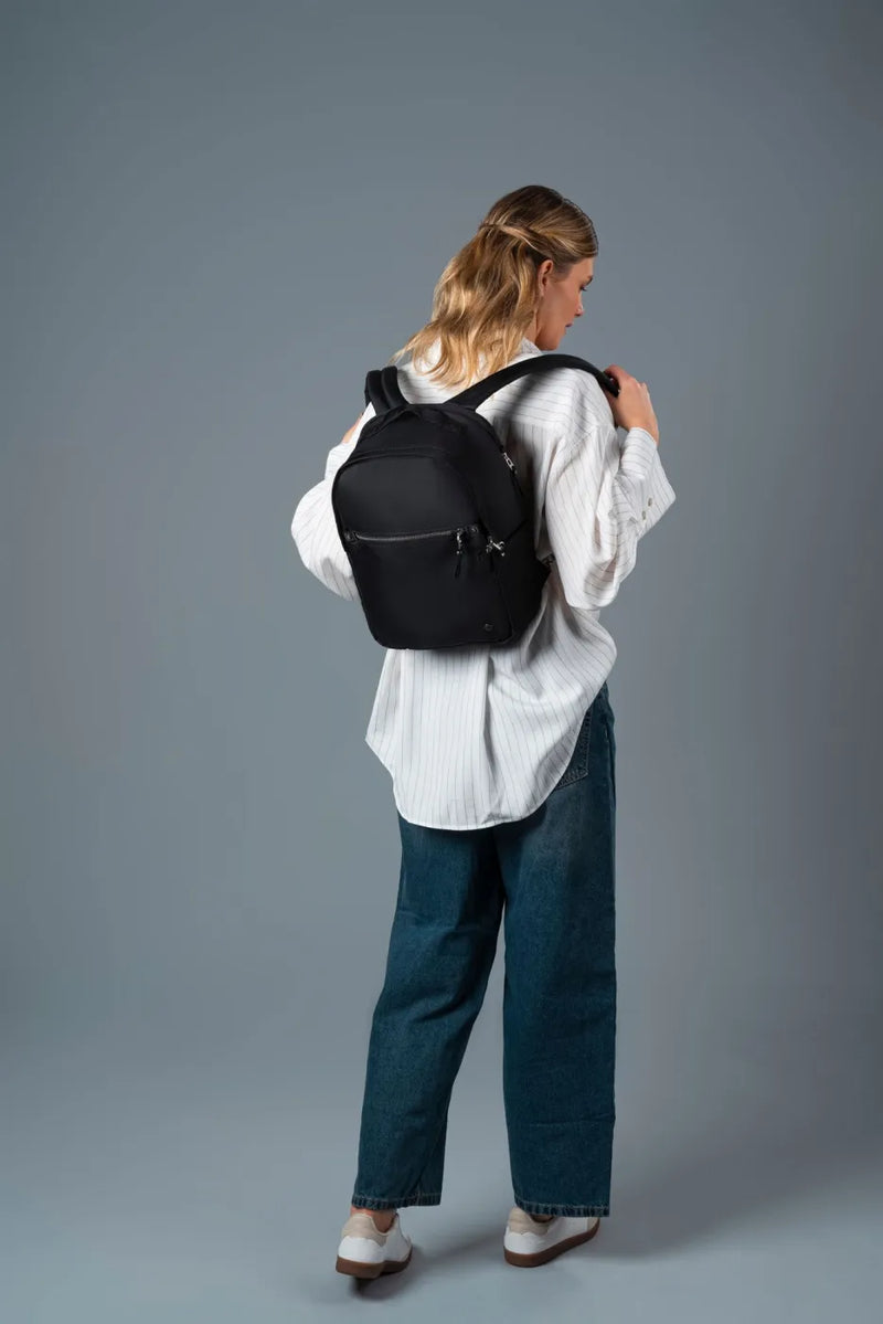 Pacsafe W 10L Anti-theft 13" Laptop Backpack in Black, swung onto the shoulders by a woman in a white shirt, seen from behind