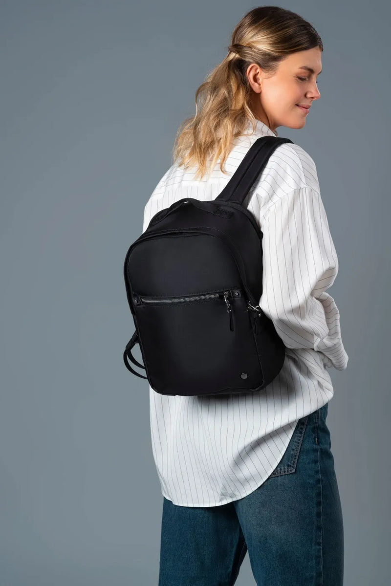 Pacsafe W 10L Anti-theft 13" Laptop Backpack in Black, worn on one shoulder by a woman in a white shirt and jeans
