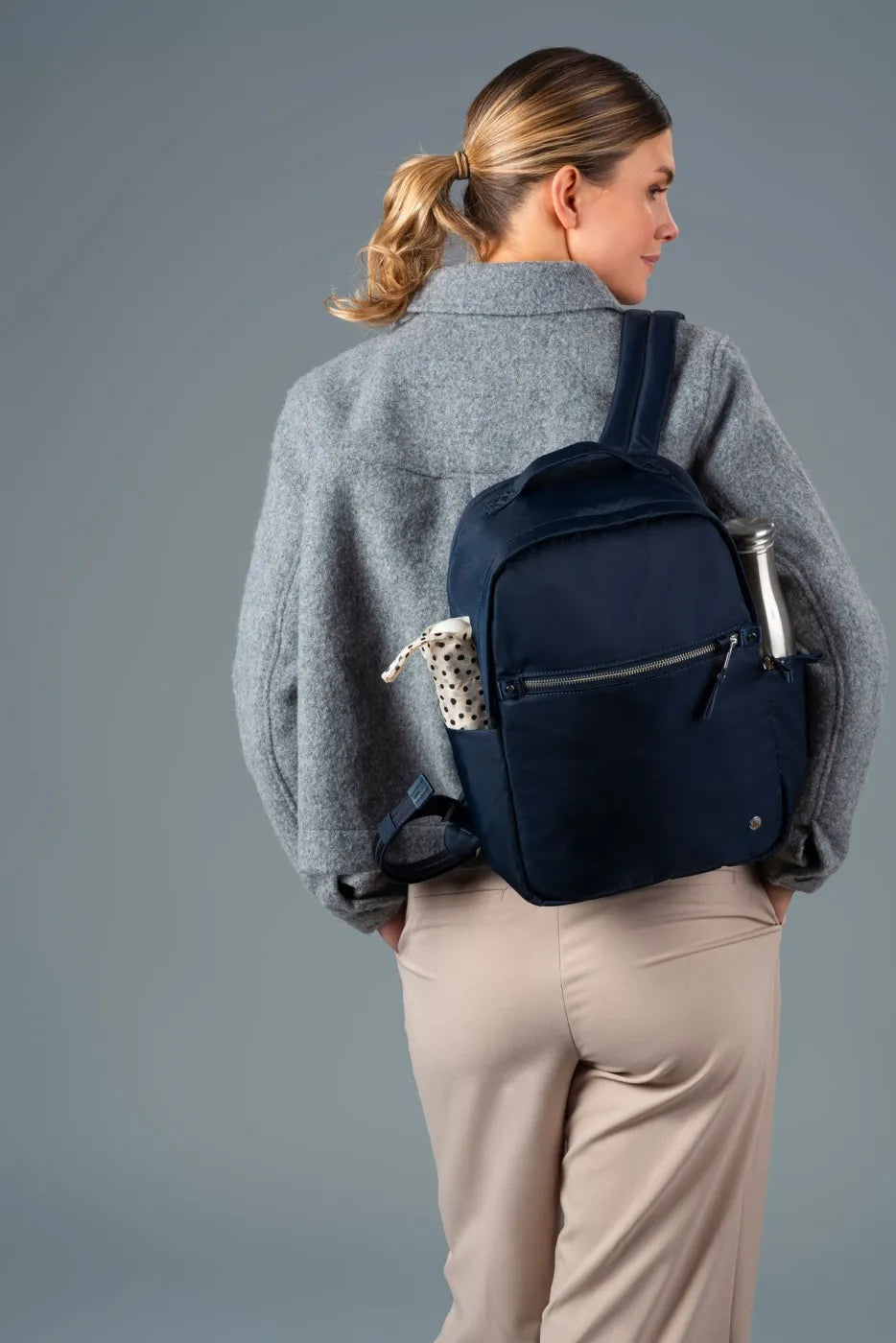 Pacsafe W 10L Anti-theft 13" Laptop Backpack in Navy, worn on both shoulders with a water bottle in the side pocket, seen from behind