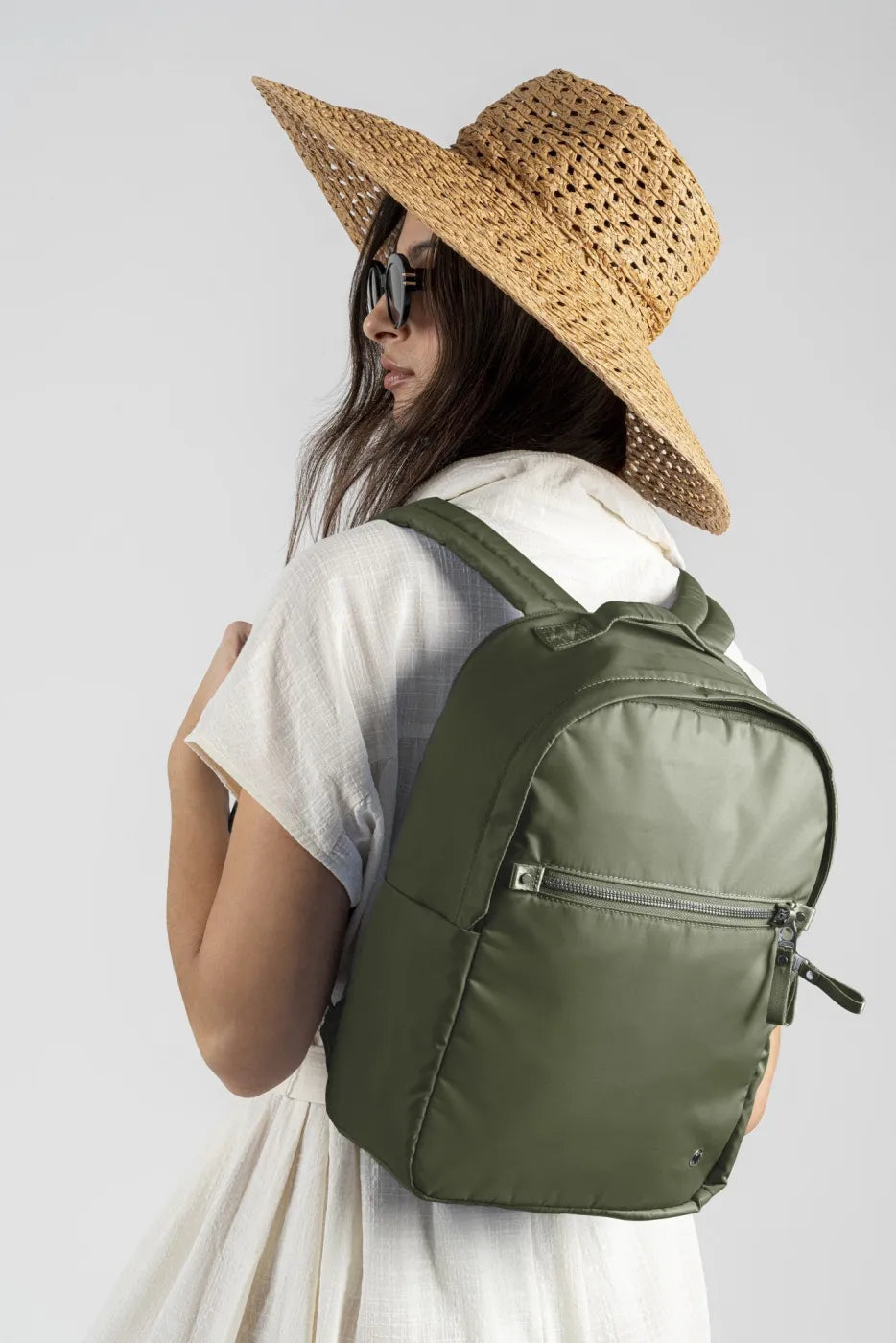 Pacsafe W 10L Anti-theft 13" Laptop Backpack in Olive, worn on one shoulder by a woman in a straw hat and white dress