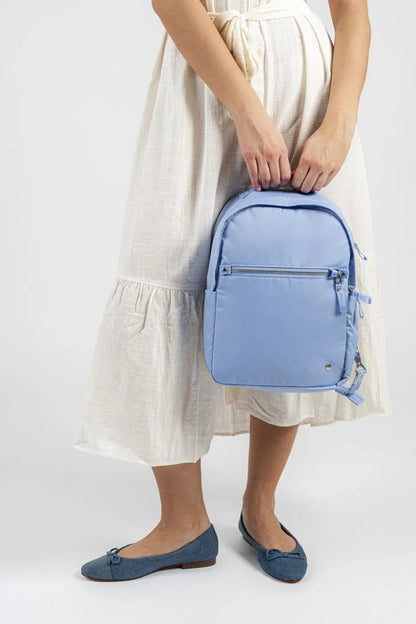 Pacsafe W 10L Anti-theft 13" Laptop Backpack in Serenity Blue, held by its grab handle at the side of a woman in a cream dress