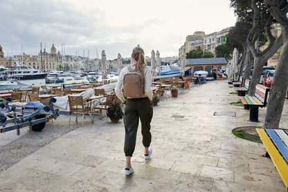 Pacsafe W 10L Anti-theft 13" Laptop Backpack in Taupe, worn on both shoulders by a woman walking a harbour promenade