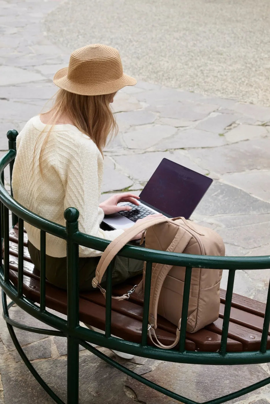 Pacsafe W 10L Anti-theft 13" Laptop Backpack in Taupe, on the bench beside a woman working on a laptop outdoors