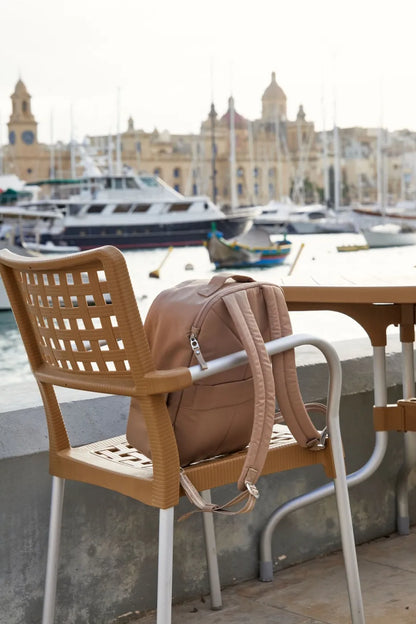 Pacsafe W 10L Anti-theft 13" Laptop Backpack in Taupe, hanging on a cafe chair at a marina, boats behind