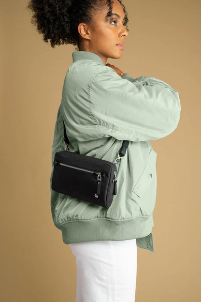 Pacsafe W Anti-theft 3-in-1 Sling Bag in Black, worn crossbody at the hip over a green bomber jacket, seen from the side