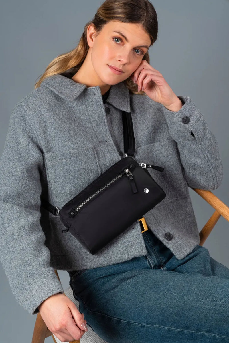 Pacsafe W Anti-theft 3-in-1 Sling Bag in Black, worn crossbody by a woman seated in a grey wool jacket