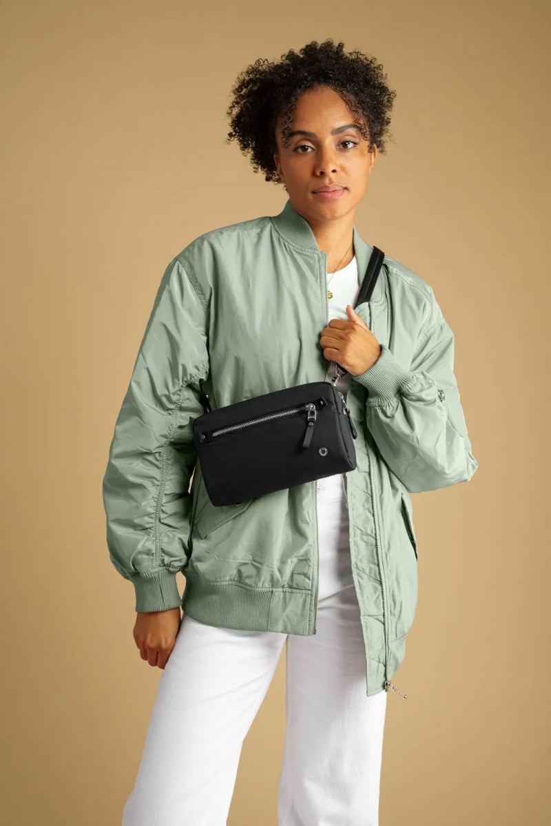 Pacsafe W Anti-theft 3-in-1 Sling Bag in Black, worn crossbody at the waist by a woman in a green bomber jacket