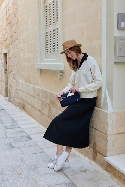Pacsafe W Anti-theft 3-in-1 Sling Bag in Navy, worn at the waist by a woman leaning against a limestone wall