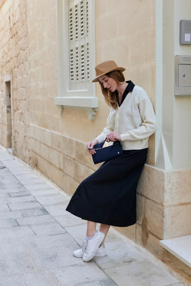 Pacsafe W Anti-theft 3-in-1 Sling Bag in Navy, worn at the waist by a woman leaning against a limestone wall