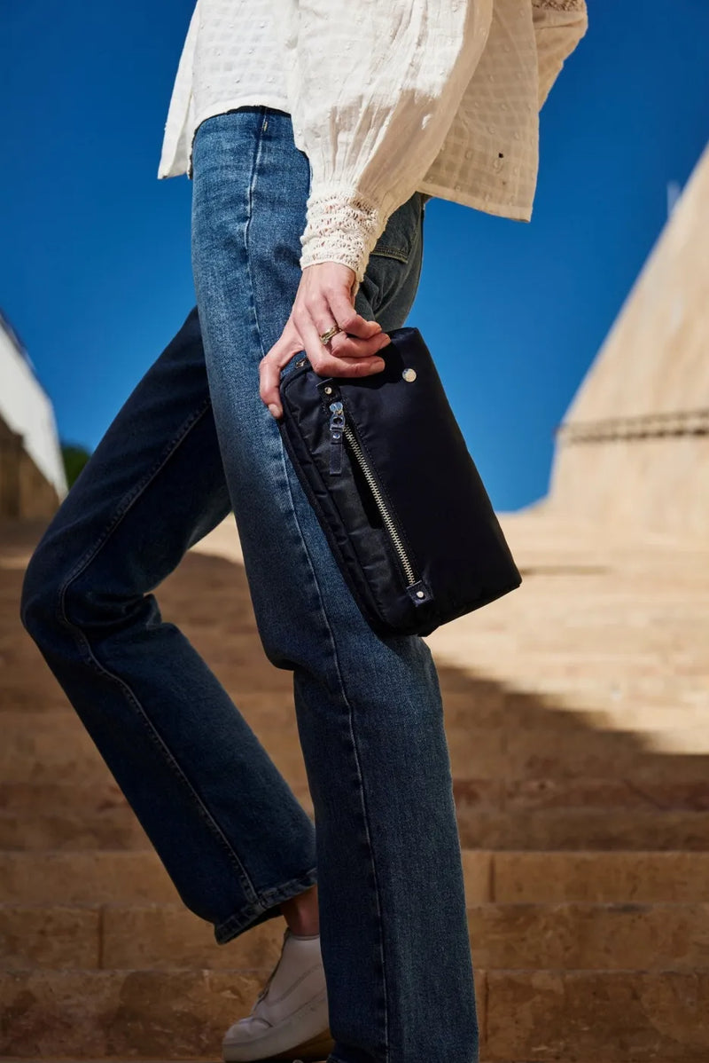 Pacsafe W Anti-theft 3-in-1 Sling Bag in Navy, carried by the strap in one hand beside a woman in jeans