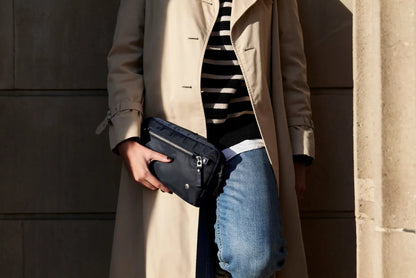 Pacsafe W Anti-theft 3-in-1 Sling Bag in Navy, carried in the hand at the hip by a woman in a trench coat