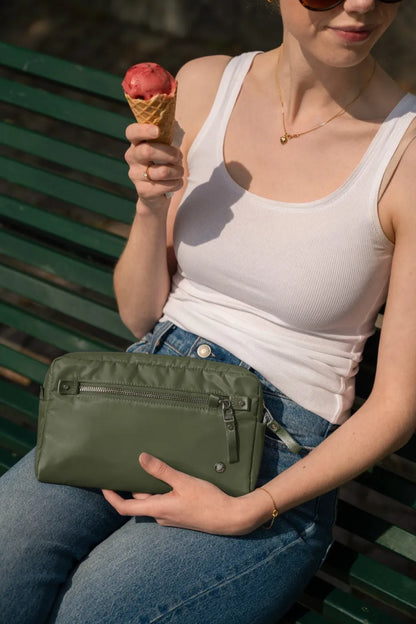 Pacsafe W Anti-theft 3-in-1 Sling Bag in Olive, held on the lap of a woman with an ice cream, sitting on a park bench