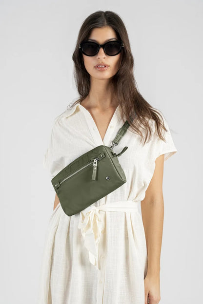 Pacsafe W Anti-theft 3-in-1 Sling Bag in Olive, worn across the chest by a woman in a cream shirt dress and sunglasses