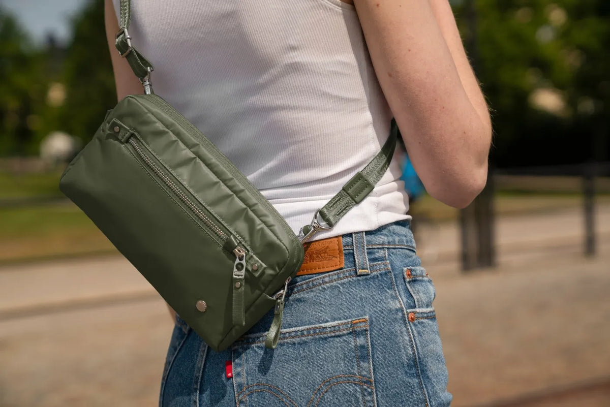 Pacsafe W Anti-theft 3-in-1 Sling Bag in Olive, worn at the back of the waist over jeans and a white tank, on a city street
