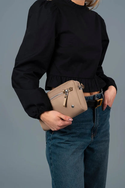 Pacsafe W Anti-theft 3-in-1 Sling Bag in Taupe, held at the hip in one hand, worn on a long strap