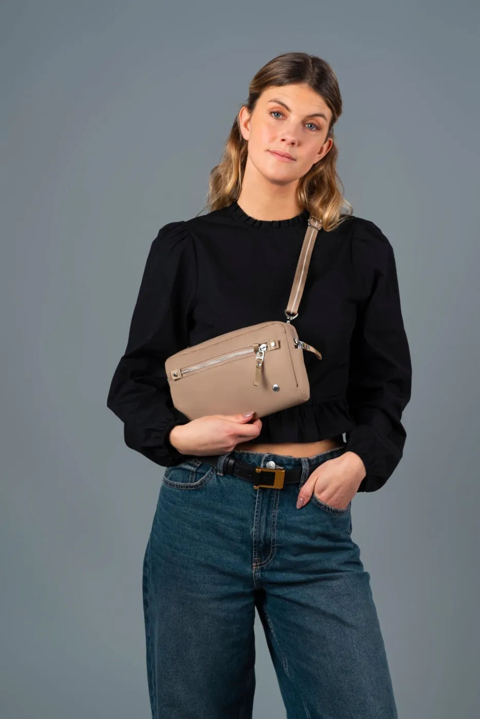 Pacsafe W Anti-theft 3-in-1 Sling Bag in Taupe, worn crossbody at chest height over a black blouse