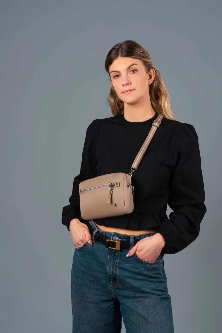 Pacsafe W Anti-theft 3-in-1 Sling Bag in Taupe, worn crossbody at the waist over a black blouse and jeans