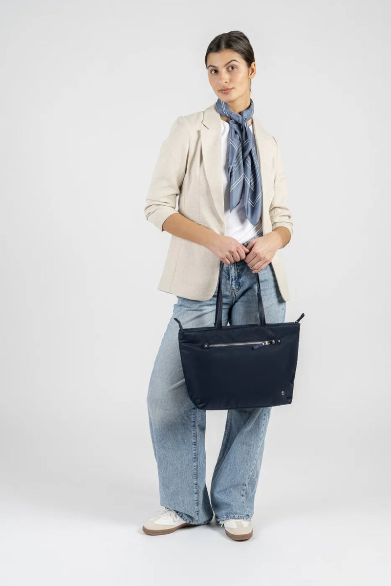 Pacsafe W Anti-theft Carryall 13" Laptop Tote in Navy, held at the side by a woman in a cream blazer and neck scarf