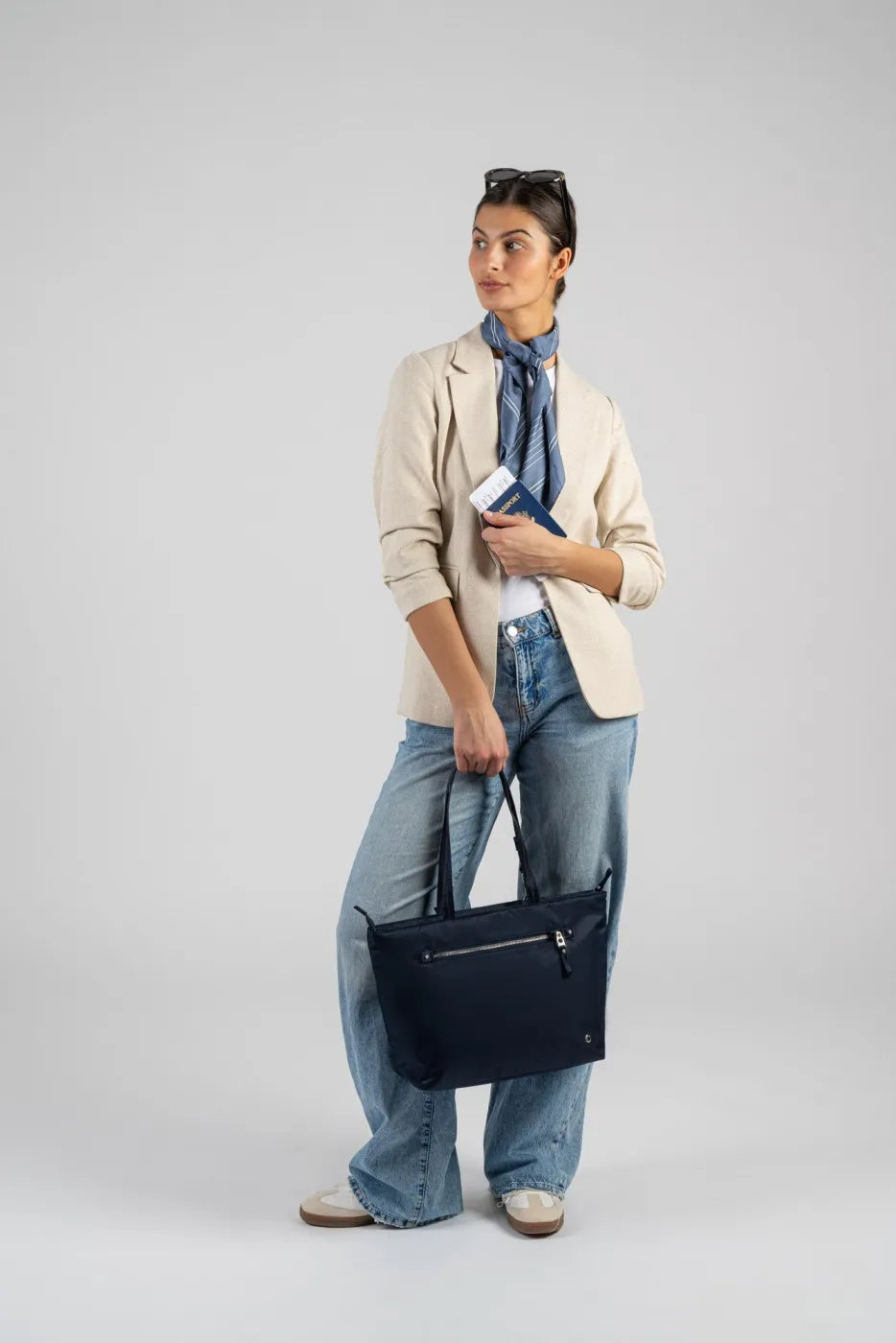 Pacsafe W Anti-theft Carryall 13" Laptop Tote in Navy, carried by its handles at the side of a woman holding a passport