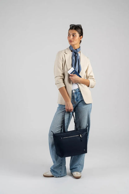 Pacsafe W Anti-theft Carryall 13" Laptop Tote in Navy, carried by its handles at the side of a woman holding a passport