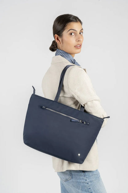 Pacsafe W Anti-theft Carryall 13" Laptop Tote in Navy, carried on the shoulder by a woman in a cream blazer, seen from the side