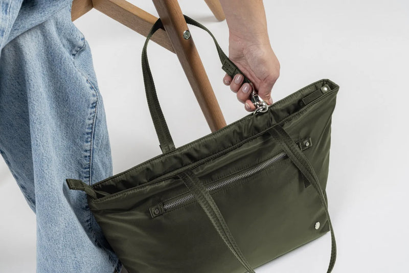 Pacsafe W Anti-theft Carryall 13" Laptop Tote in Olive, lifted by its shoulder straps beside a wooden chair