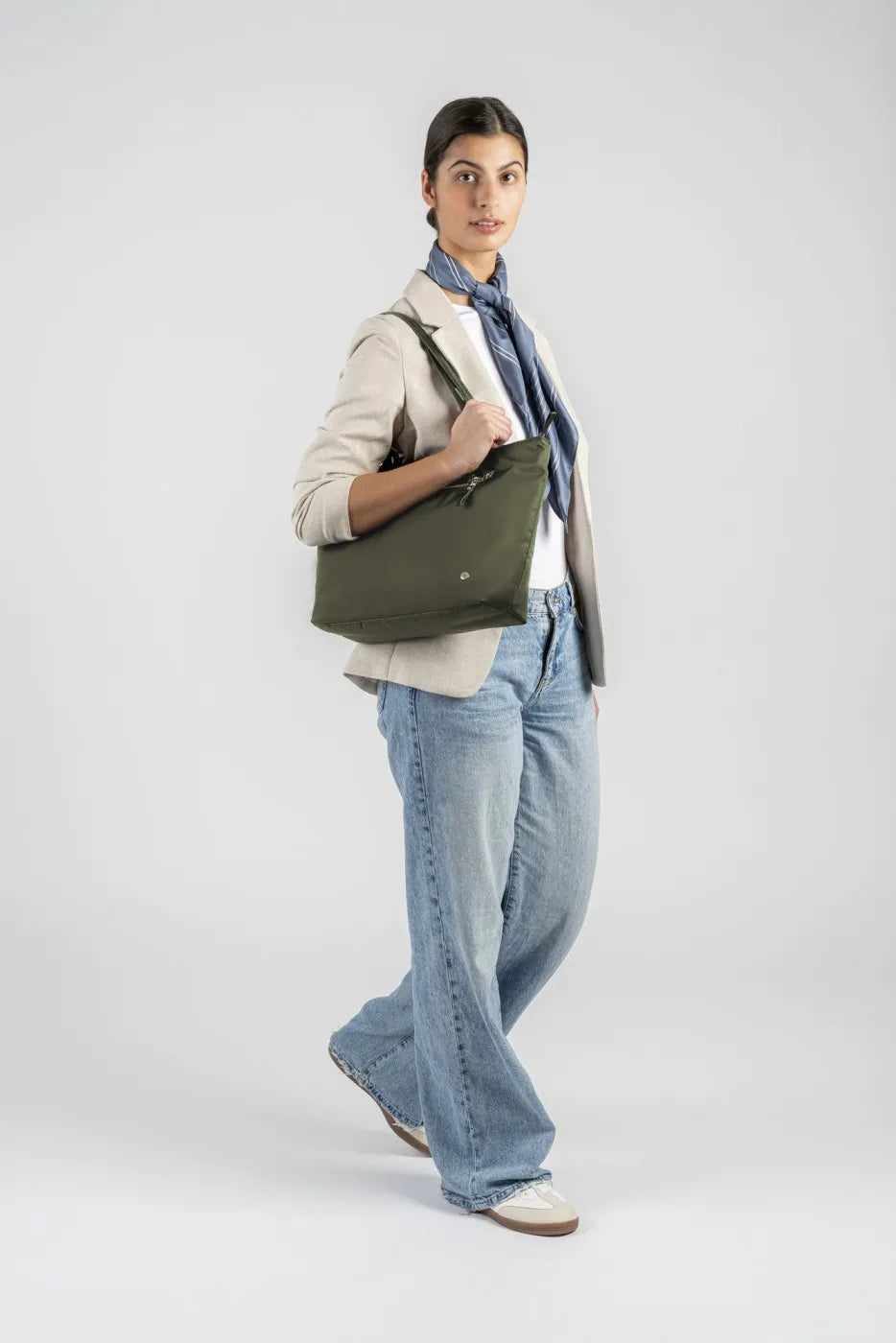 Pacsafe W Anti-theft Carryall 13" Laptop Tote in Olive, carried over the shoulder by a woman walking in a cream blazer and wide leg jeans