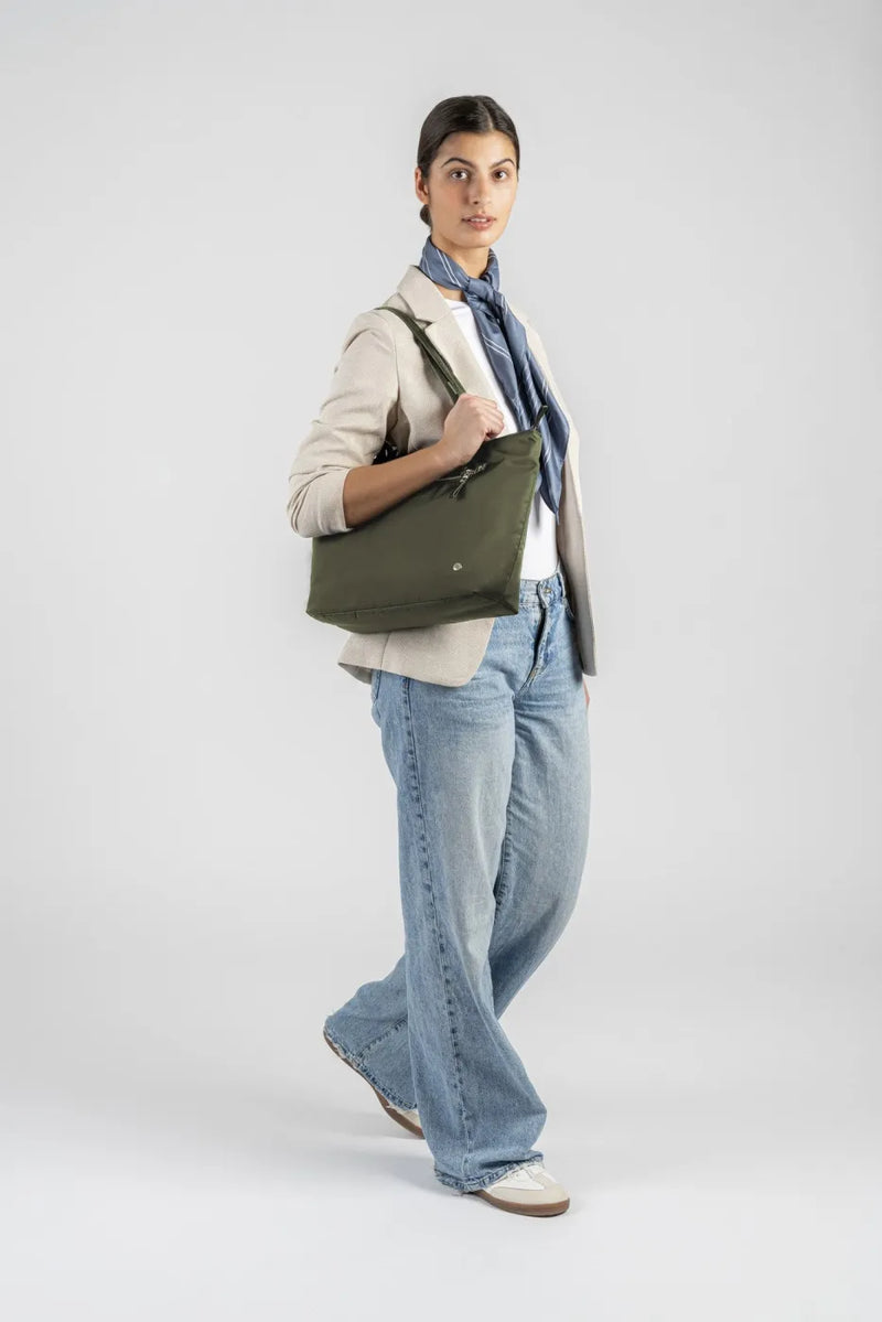 Pacsafe W Anti-theft Carryall 13" Laptop Tote in Olive, carried over the shoulder by a woman walking in a cream blazer and wide leg jeans