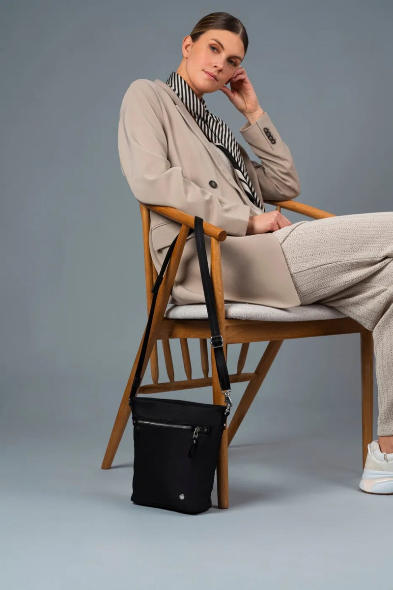 Pacsafe W Anti-theft Crossbody Bag in Black, hanging from the back of a chair beside a seated woman
