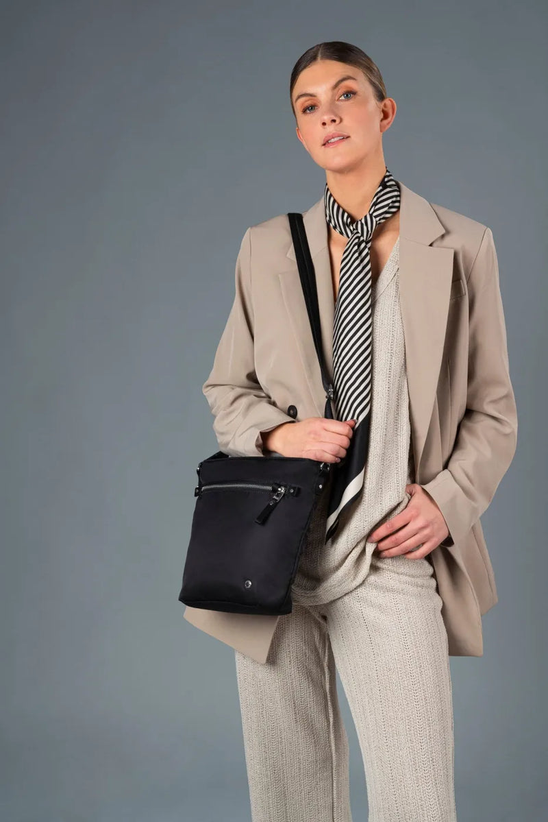 Pacsafe W Anti-theft Crossbody Bag in Black, worn crossbody by a woman in a beige blazer and neck scarf