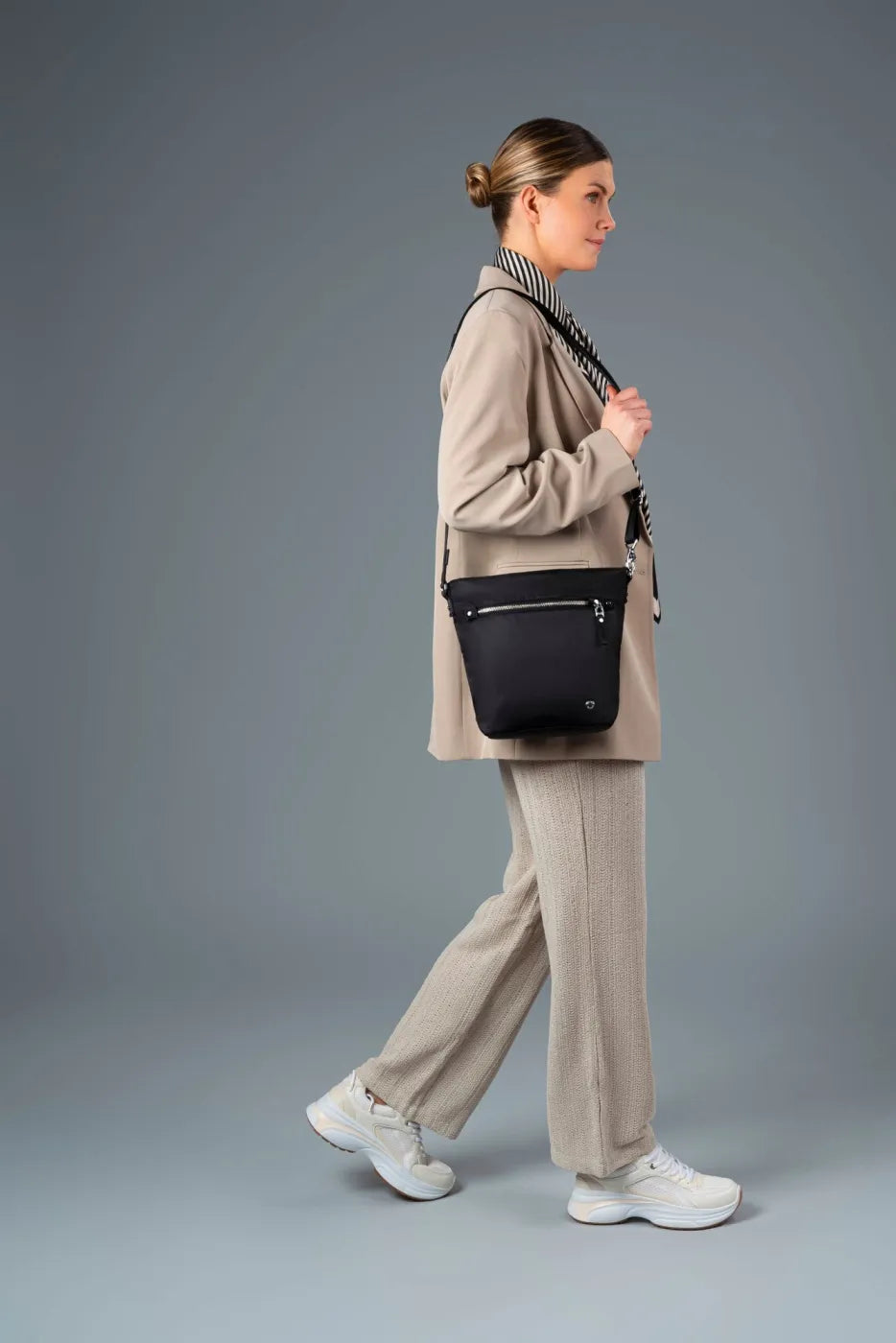 Pacsafe W Anti-theft Crossbody Bag in Black, worn crossbody by a woman walking in a linen suit