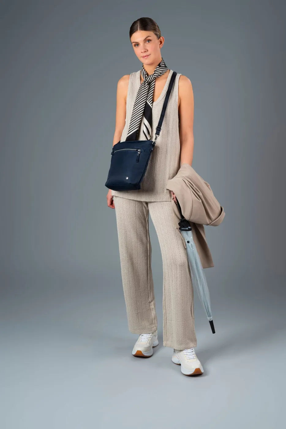 Pacsafe W Anti-theft Crossbody Bag in Navy, worn crossbody by a woman carrying a coat and umbrella