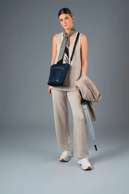 Pacsafe W Anti-theft Crossbody Bag in Navy, worn crossbody by a woman carrying a coat and umbrella