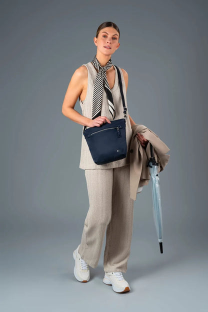 Pacsafe W Anti-theft Crossbody Bag in Navy, worn crossbody by a woman in a linen suit, coat over her arm