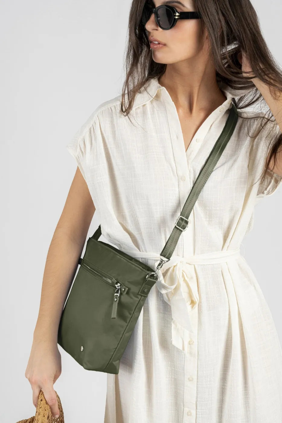 Pacsafe W Anti-theft Crossbody Bag in Olive, worn on a shortened crossbody strap by a woman in a cream shirt dress