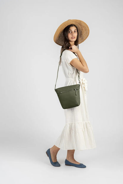 Pacsafe W Anti-theft Crossbody Bag in Olive, worn at hip height on a long strap by a woman in a cream dress and straw hat