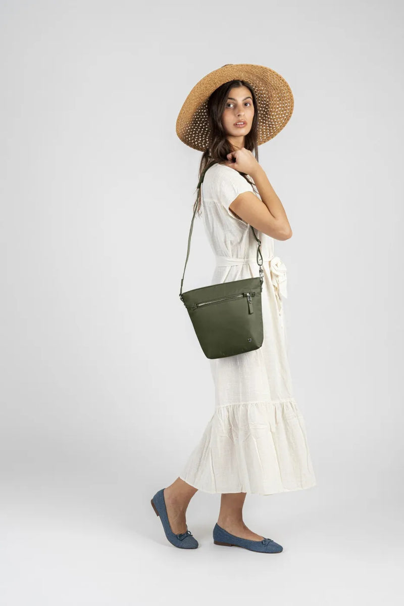 Pacsafe W Anti-theft Crossbody Bag in Olive, worn at hip height on a long strap by a woman in a cream dress and straw hat