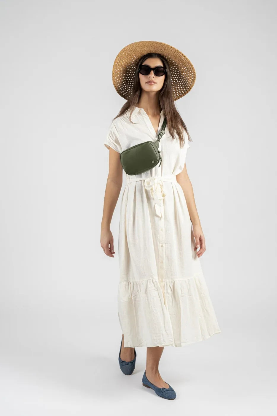 Pacsafe W Anti-theft Micro Sling in Olive, worn across the waist by a woman in a cream linen dress and straw sun hat
