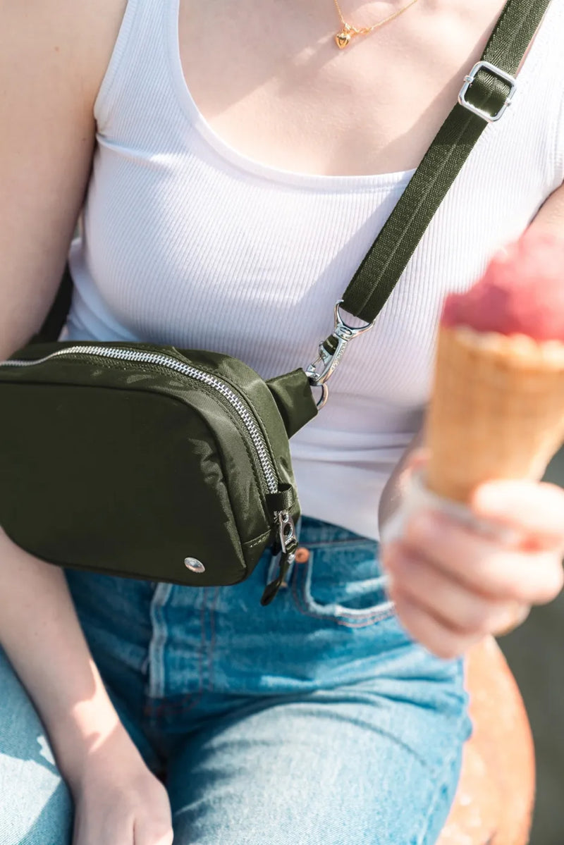 Pacsafe W Anti-theft Micro Sling in Olive, close up of the bag at the hip on its wide webbing strap, ice cream in hand