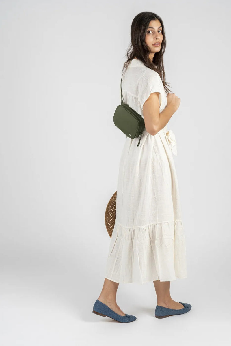 Pacsafe W Anti-theft Micro Sling in Olive, worn at the hip by a woman in a cream linen dress, seen from the side