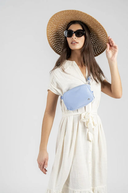 Pacsafe W Anti-theft Micro Sling in Serenity Blue, worn at the waist by a woman in a cream dress and wide straw hat